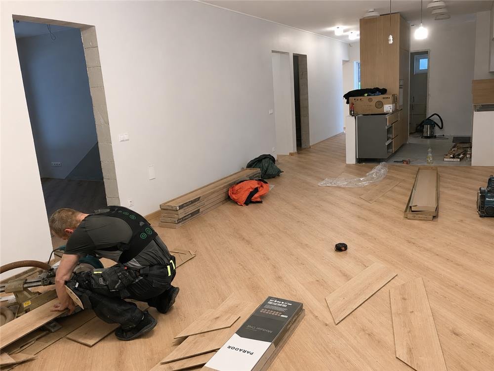 Installer fitting oak plank flooring in a residential living area